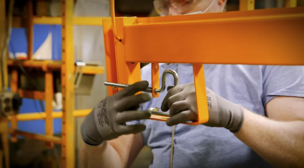 A worker threads a curved hook bolt into place on scaffolding.